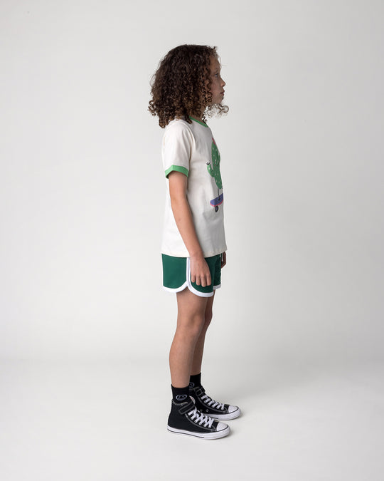Kid wearing the Skate Cactus Tee in cream and green with the Sprint Short in kelly green and white, side view