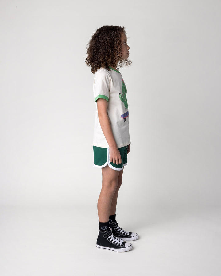 Kid wearing the Skate Cactus Tee in cream and green with the Sprint Short in kelly green and white, side view