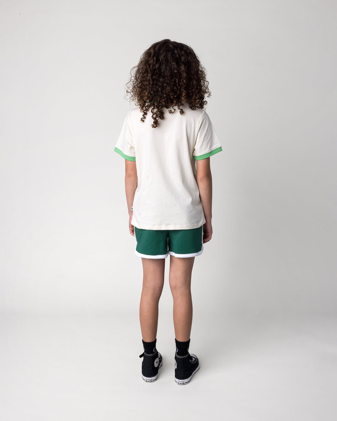 Kid wearing the Skate Cactus Tee in cream and green with the Sprint Short in kelly green and white, back view