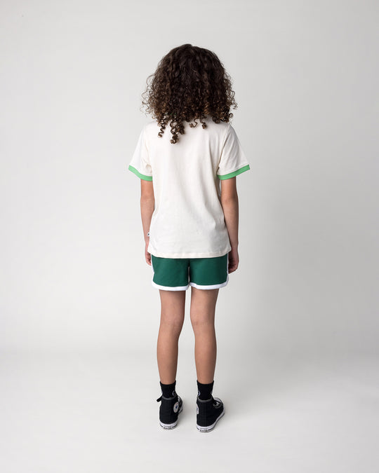 Kid wearing the Skate Cactus Tee in cream and green with the Sprint Short in kelly green and white, back view