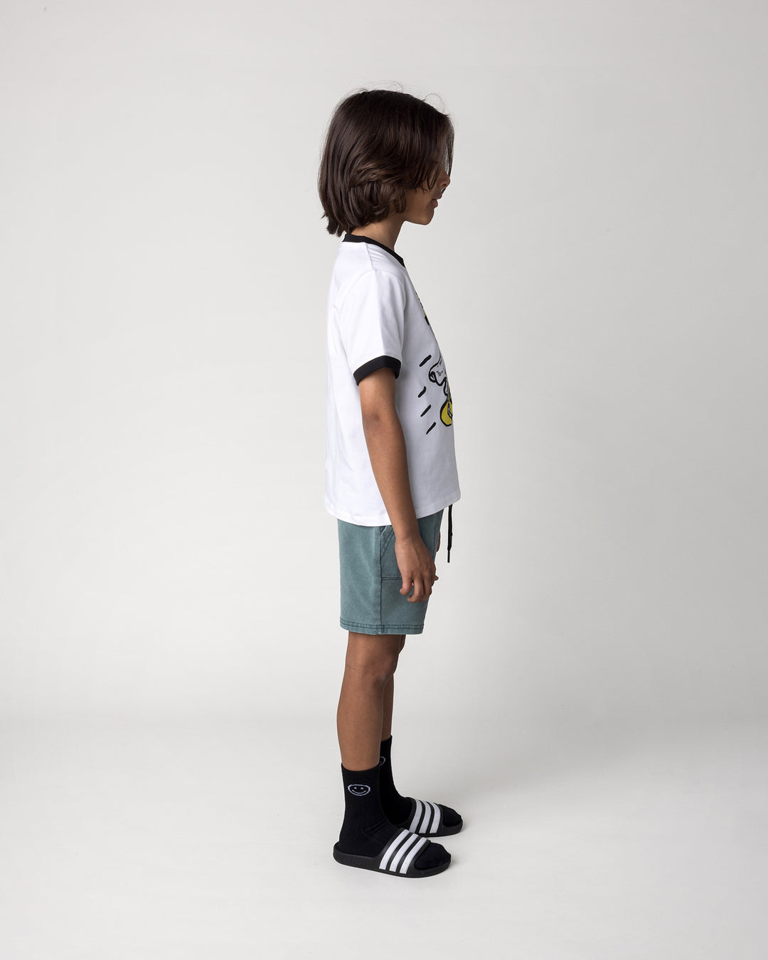 Kid wearing the Skate Ghost Tee in white and black with the Blasted Track Short in forest wash, side view