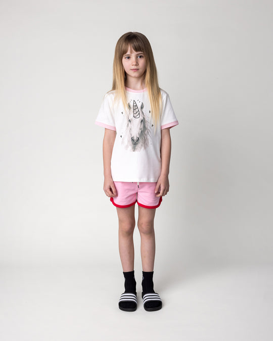 Kid wearing the Watercolour Unicorn Tee in white and pink with the Sprint Short in pink and red, front view