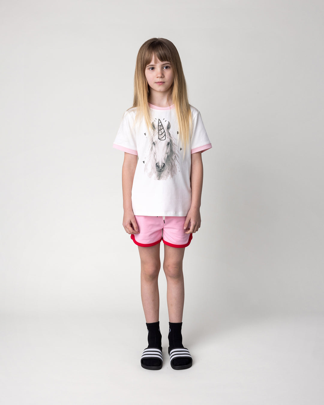Kid wearing the Watercolour Unicorn Tee in white and pink with the Sprint Short in pink and red, front view