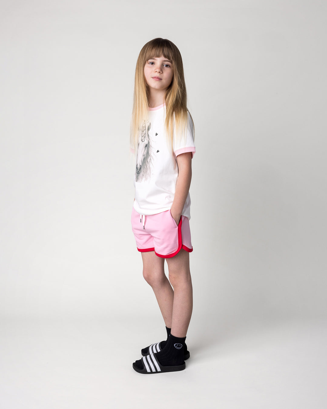 Kid wearing the Watercolour Unicorn Tee in white and pink with the Sprint Short in pink and red, side view