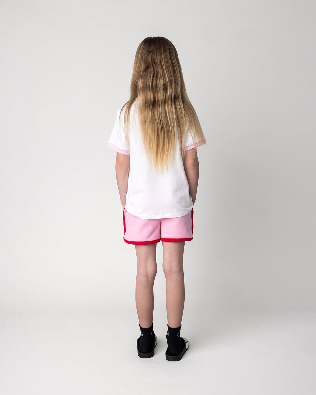 Kid wearing the Watercolour Unicorn Tee in white and pink with the Sprint Short in pink and red, back view