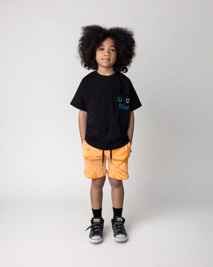 Kid wearing the Badges Tee in black with the Splatter Short in orange, front view