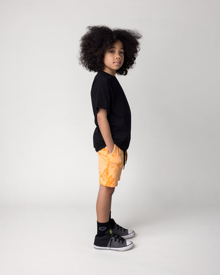 Kid wearing the Badges Tee in black with the Splatter Short in orange, side view
