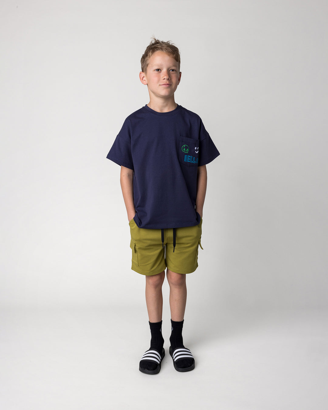 Kid wearing the Badges Tee in ink with the Deluxe Cargo Short in olive, front view