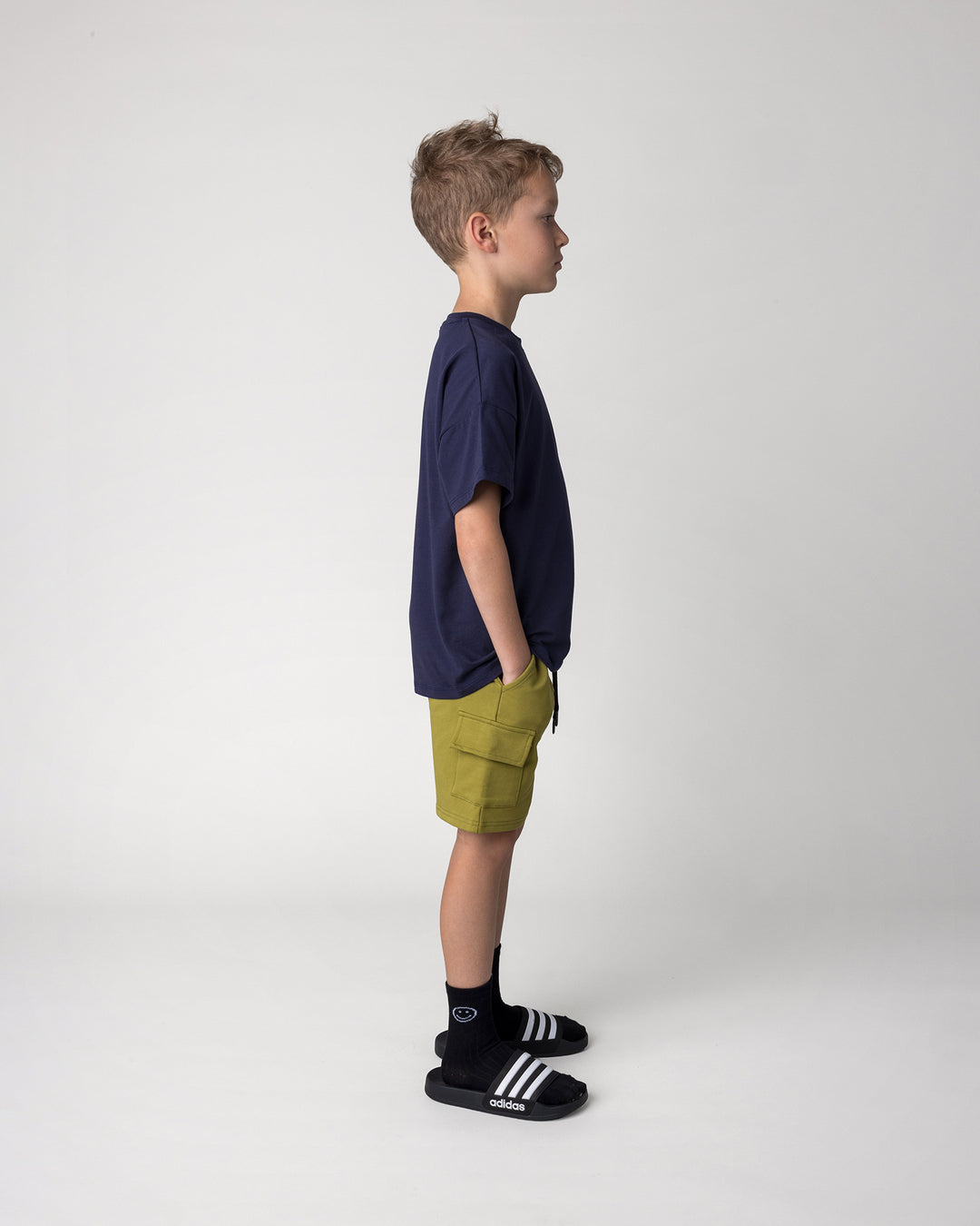 Kid wearing the Badges Tee in ink with the Deluxe Cargo Short in olive, side view
