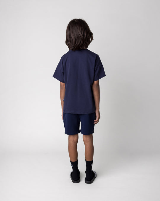 Kid wearing the Badges Tee in ink with the Badges Short in ink, back view
