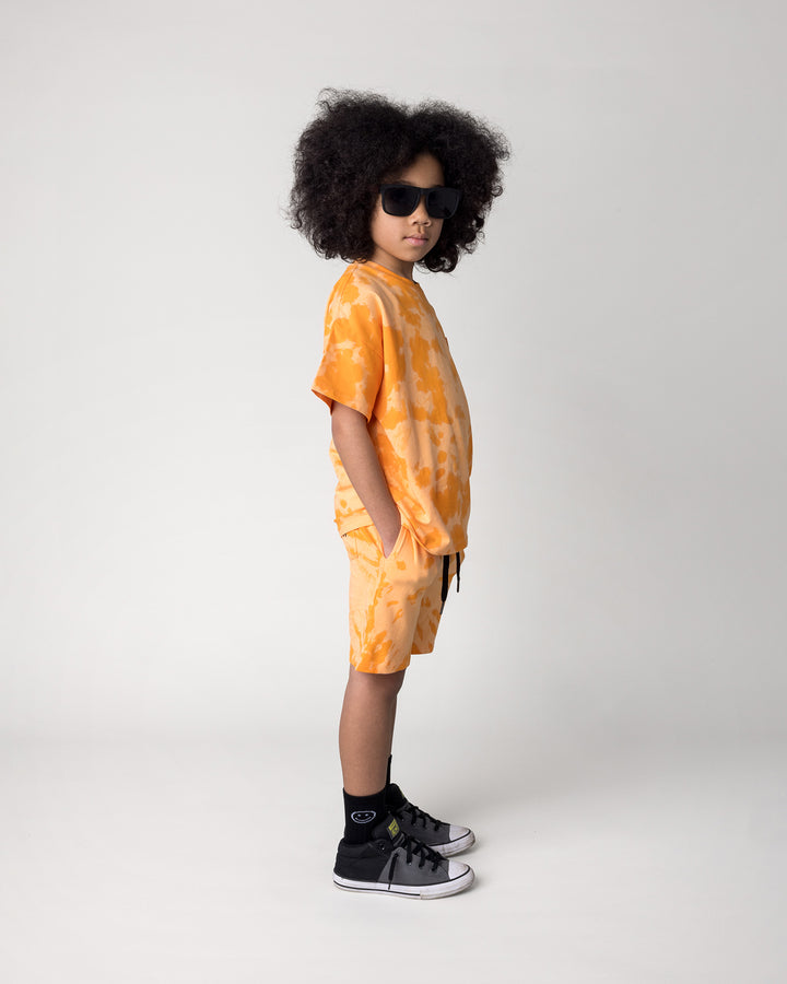 Kid wearing the Splatter Tee in orange with the Splatter Short in orange, side view