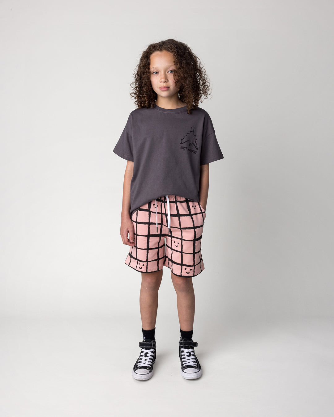 Kid wearing the Happy Squares Short in dusty pink with the Just Hanging Tee in dark grey, front view