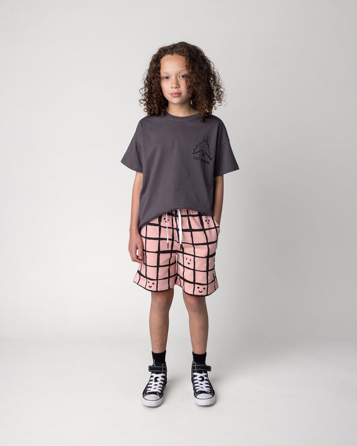 Kid wearing the Happy Squares Short in dusty pink with the Just Hanging Tee in dark grey, front view