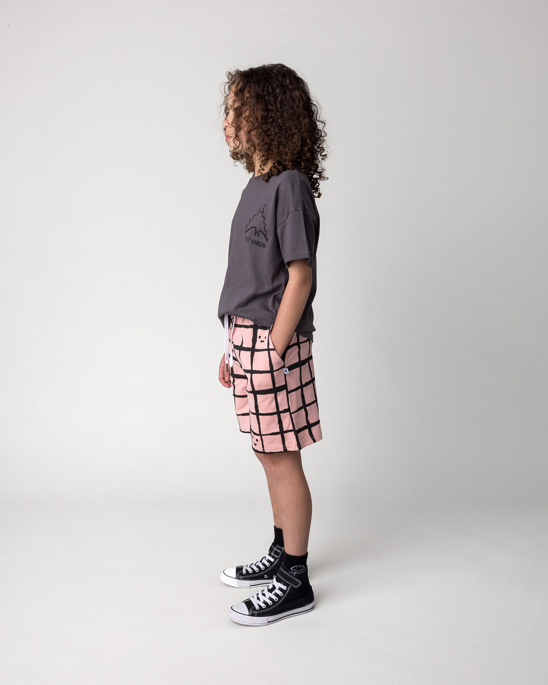 Kid wearing the Happy Squares Short in dusty pink with the Just Hanging Tee in dark grey, side view