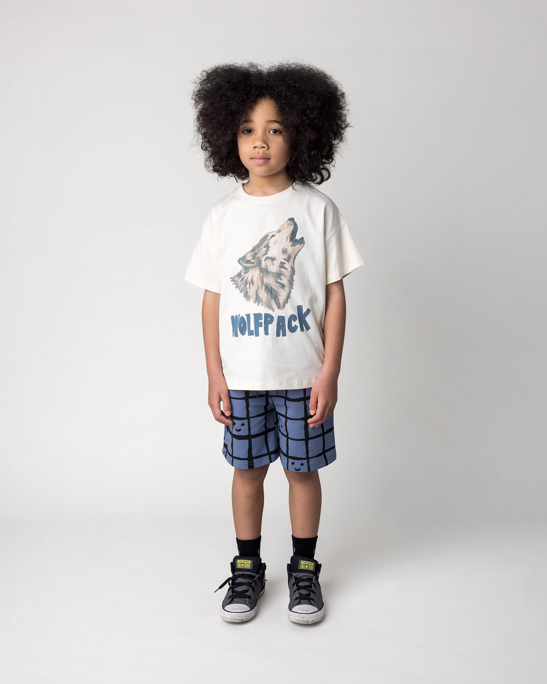 Kid wearing the Happy Squares Short in muted blue with the Wolfpack Tee in cream, front view