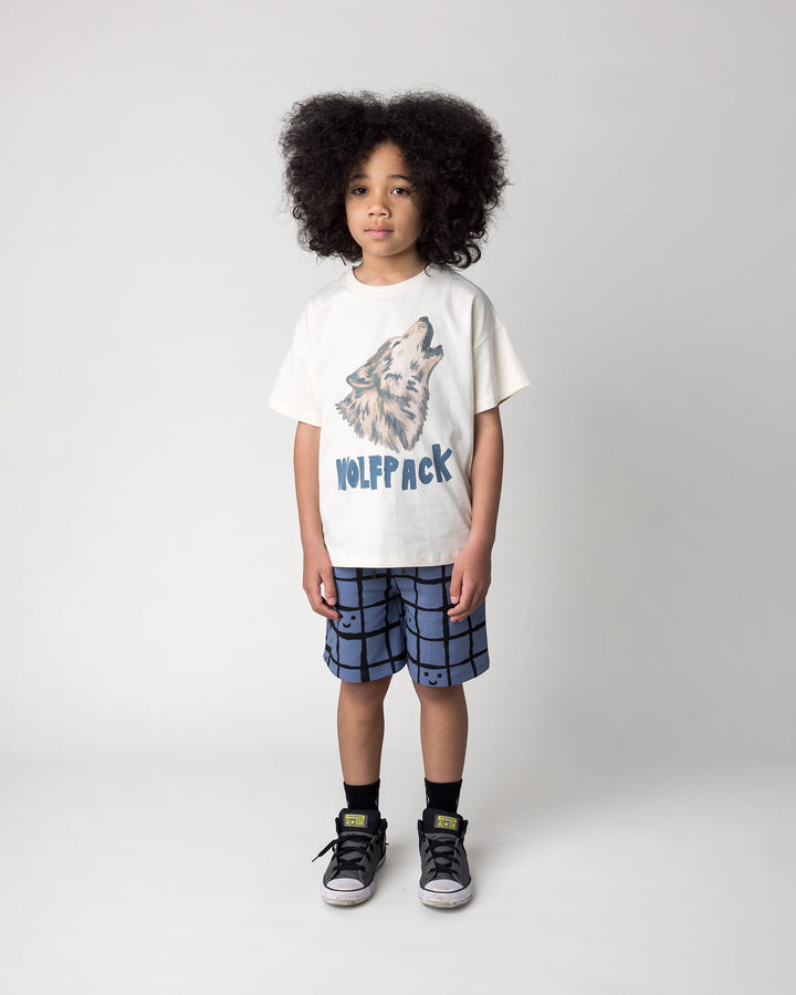Kid wearing the Happy Squares Short in muted blue with the Wolfpack Tee in cream, front view