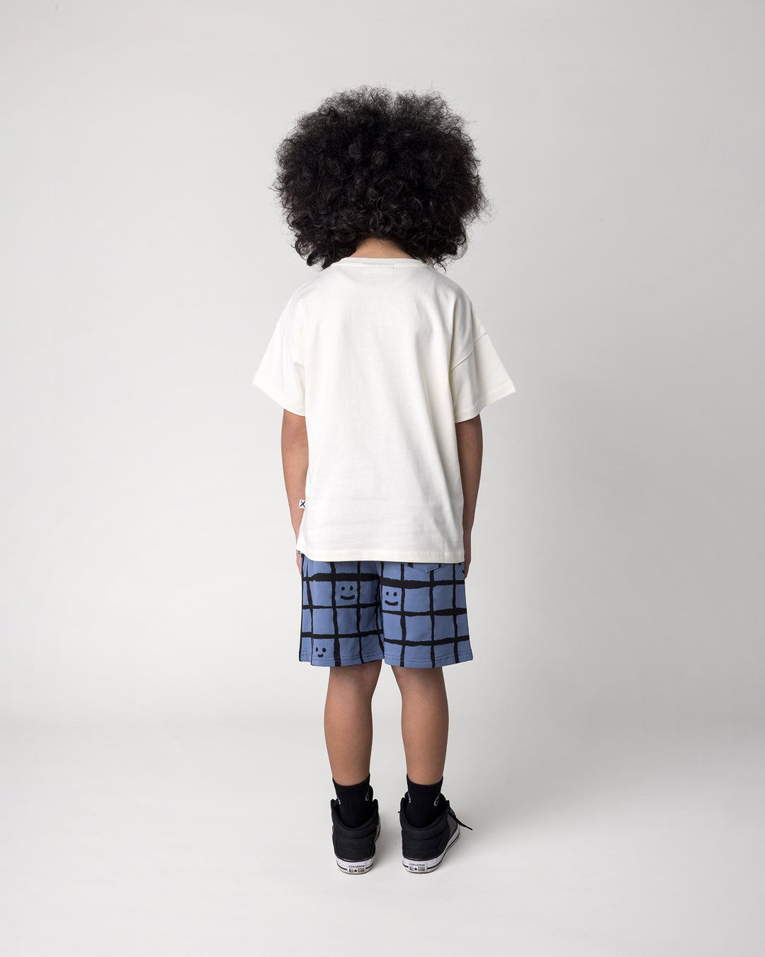 Kid wearing the Happy Squares Short in muted blue with the Wolfpack Tee in cream, back view