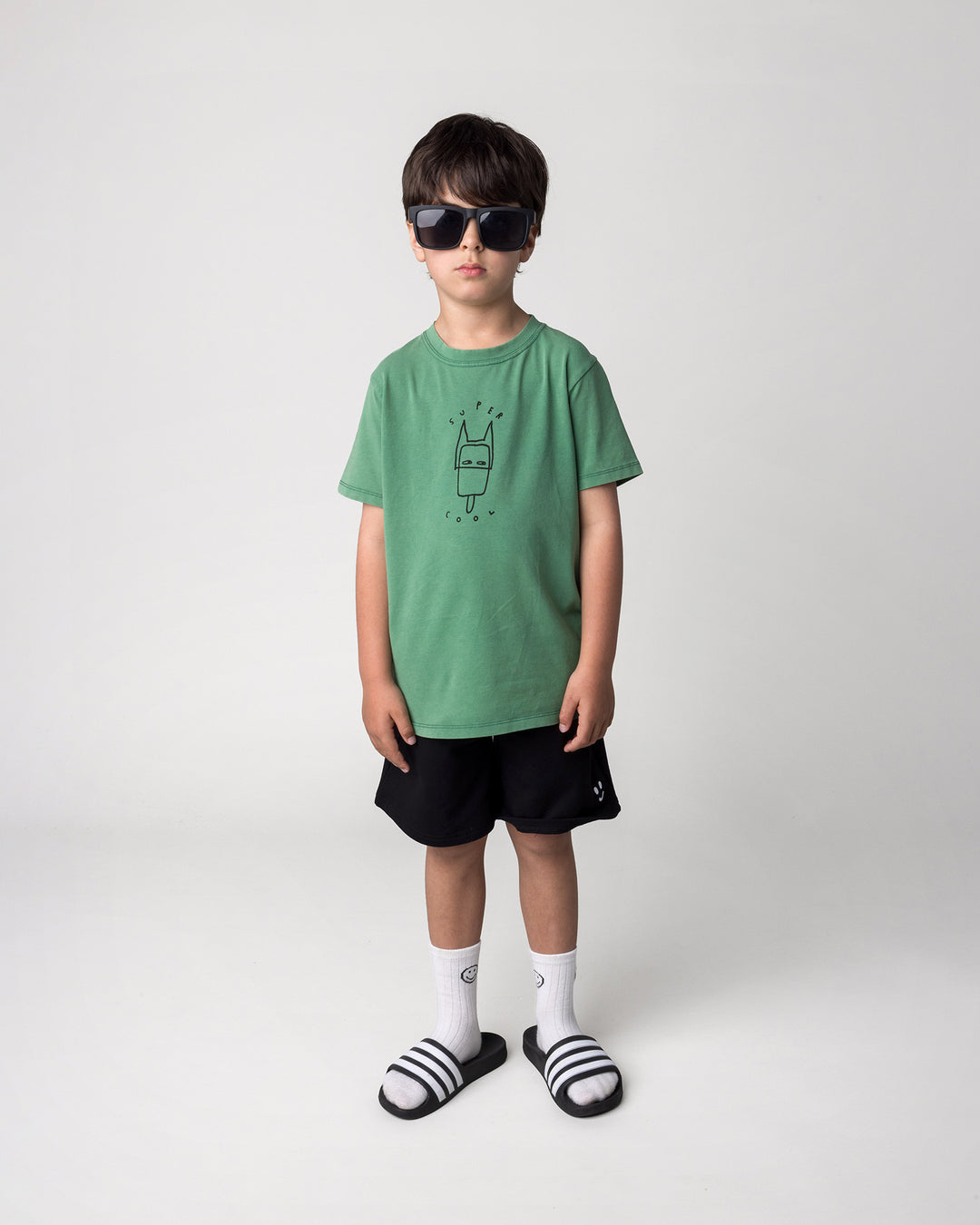 Kid wearing the Smile Short in black with the Super Cool Tee in turf wash, front view