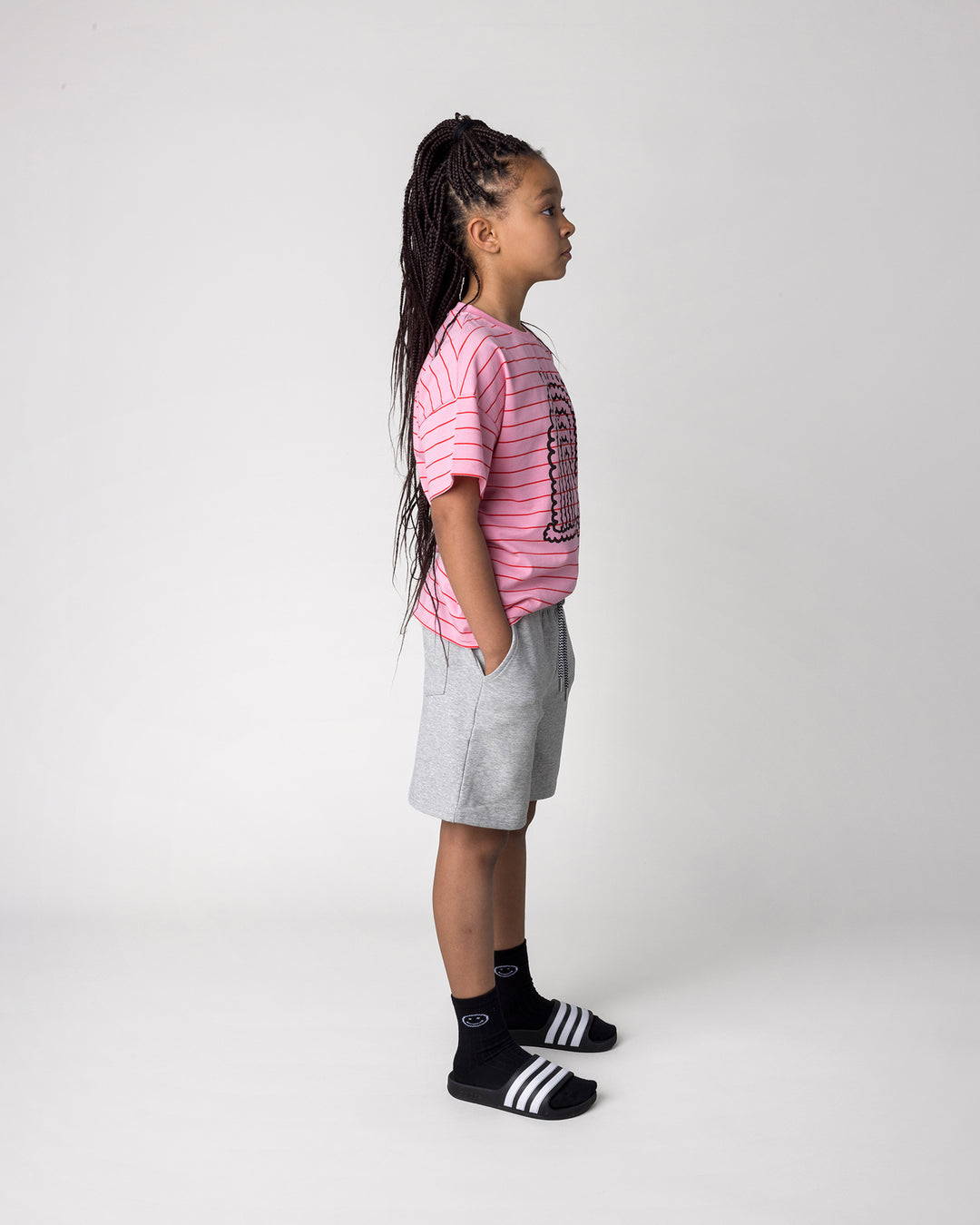 Kid wearing the Smile Short in grey marle with the Happy Rainbow Tee in pink and red stripe, side view
