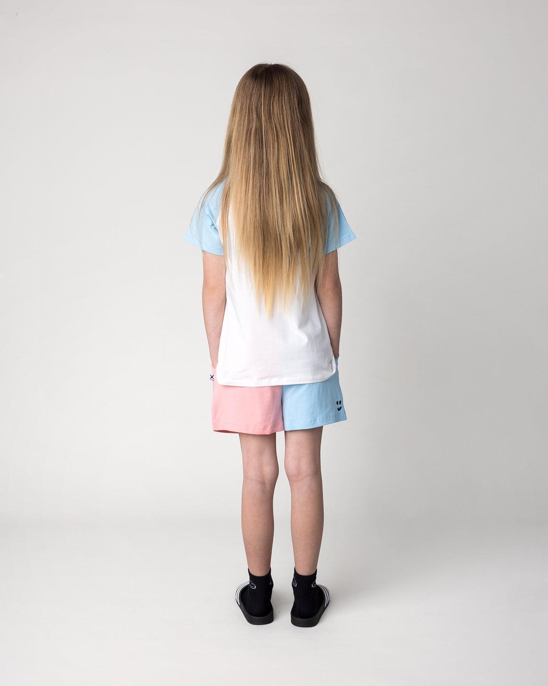 Kid wearing the Daydreaming Unicorn Tee in white and light blue with the Two Tone Short in light blue and pink, back view