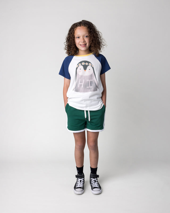 Kid wearing the Flower Penguin Tee in white, ink and yellow with the Sprint Short in kelly green and white, front view