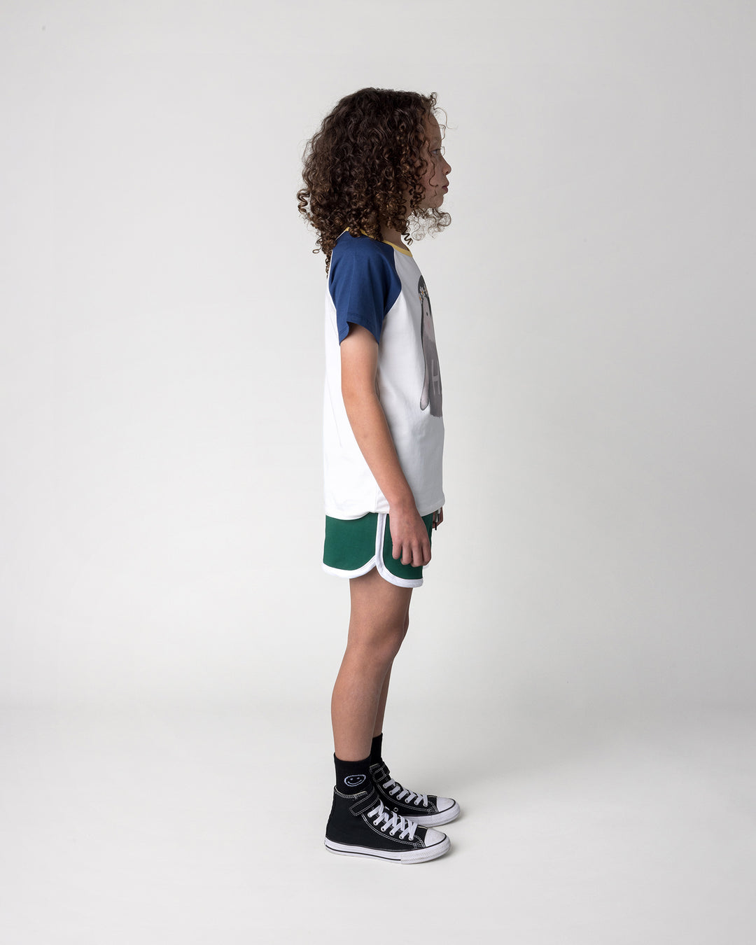 Kid wearing the Flower Penguin Tee in white, ink and yellow with the Sprint Short in kelly green and white, side view