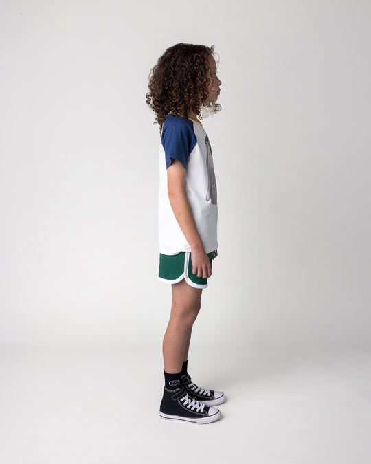 Kid wearing the Flower Penguin Tee in white, ink and yellow with the Sprint Short in kelly green and white, side view