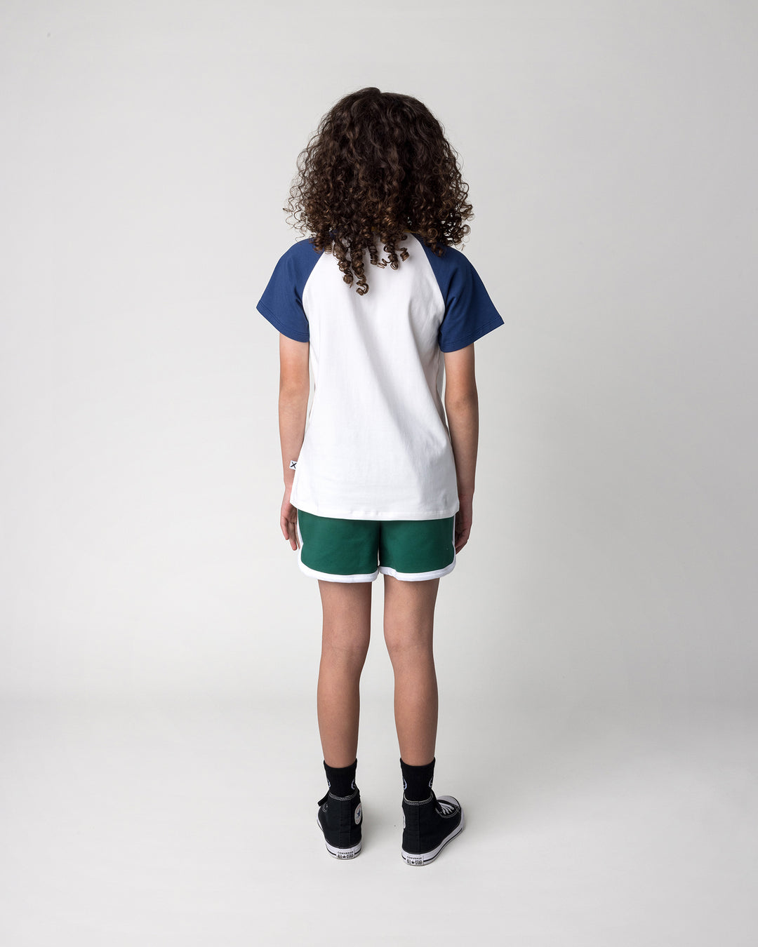 Kid wearing the Flower Penguin Tee in white, ink and yellow with the Sprint Short in kelly green and white, back view