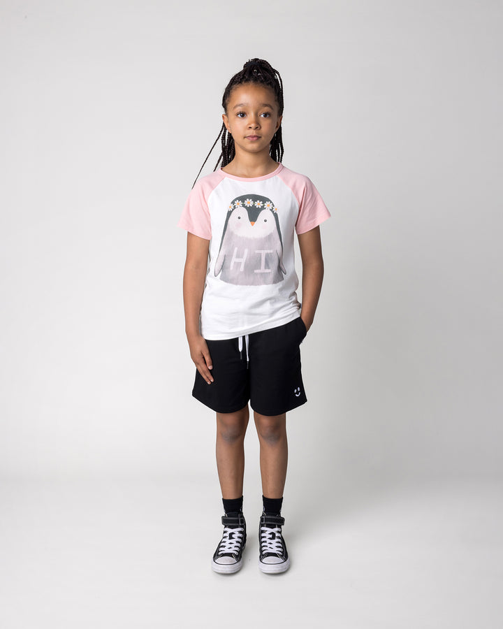 Kid wearing the Flower Penguin Tee in white and pink with the Smile Short in black, front view