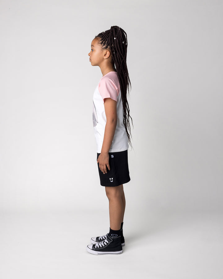 Kid wearing the Flower Penguin Tee in white and pink with the Smile Short in black, side view