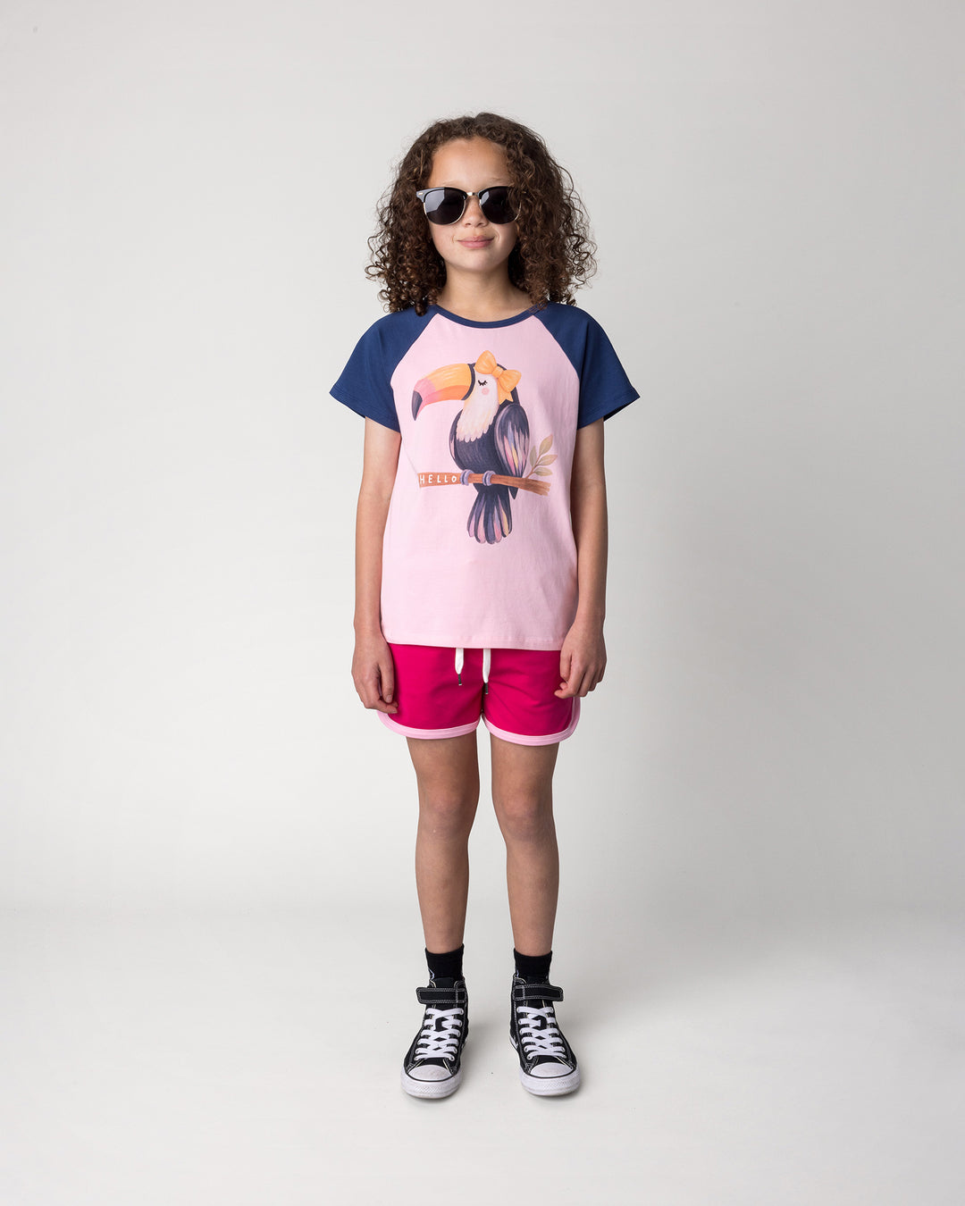 Kid wearing the Hello Toucan Tee in ballet and ink with the Sprint Short in crimson and pink, front view