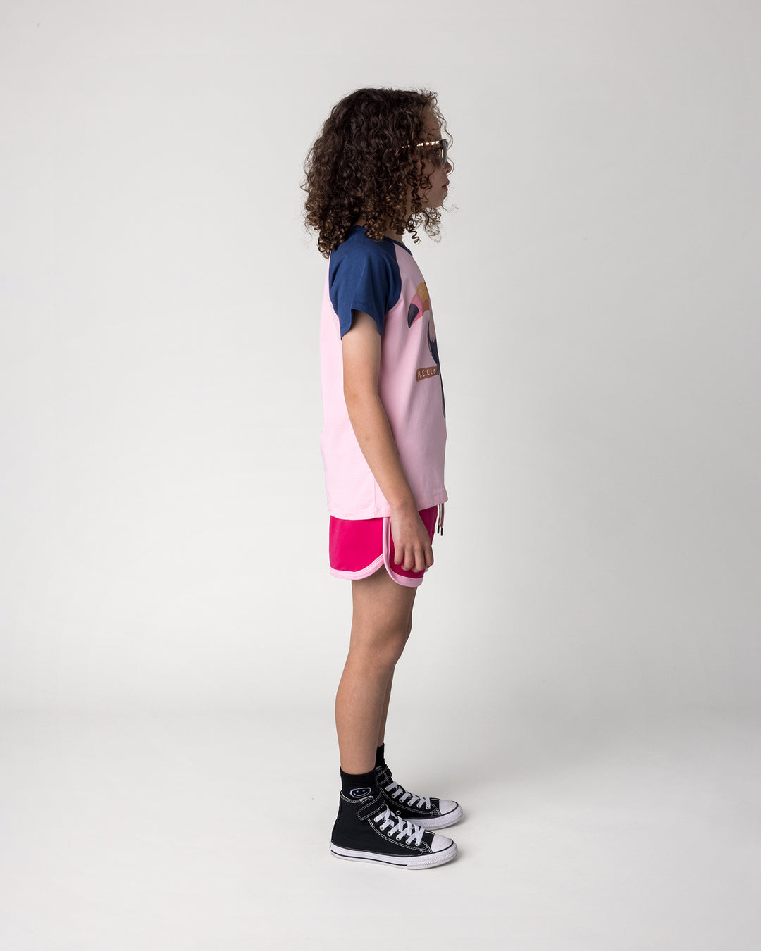 Kid wearing the Hello Toucan Tee in ballet and ink with the Sprint Short in crimson and pink, side view