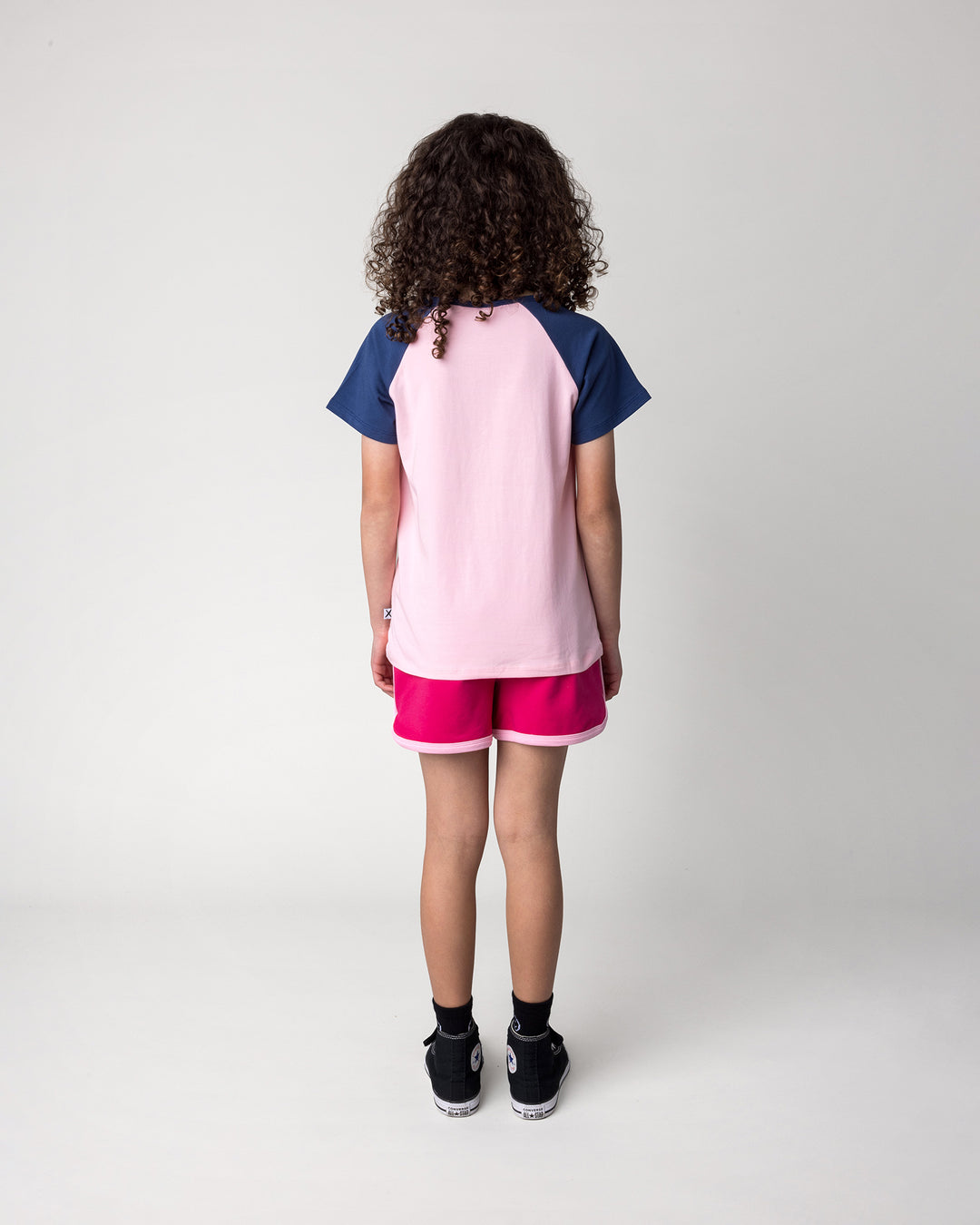Kid wearing the Hello Toucan Tee in ballet and ink with the Sprint Short in crimson and pink, back view