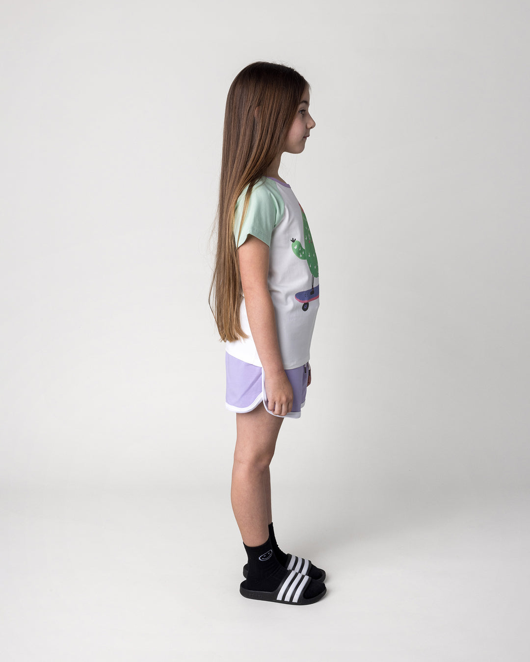 Kid wearing the Skate Cactus Tee in white and mint with the Sprint Short in lilac and white, side view