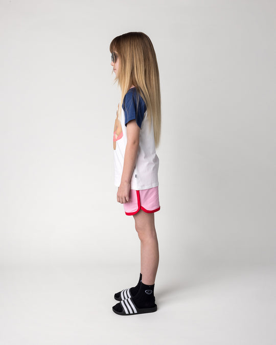 Kid wearing the Swimming Sloth Tee in white, ink and pink with the Sprint Short in pink and red, side view