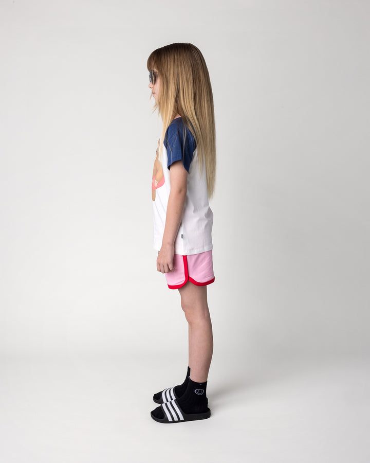 Kid wearing the Swimming Sloth Tee in white, ink and pink with the Sprint Short in pink and red, side view