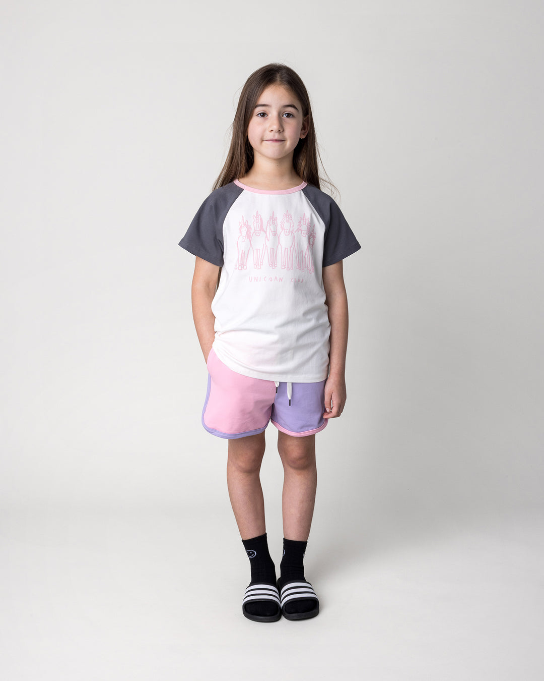 Kid wearing the Unicorn Club Tee in white and dark grey with the Sprint Short in pink, purple and aqua, front view