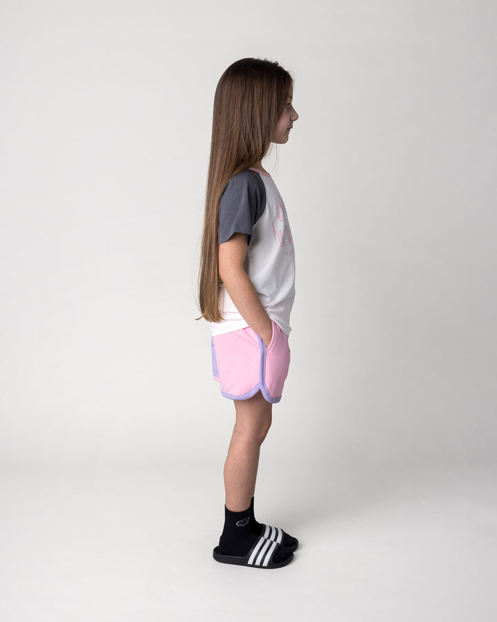 Kid wearing the Unicorn Club Tee in white and dark grey with the Sprint Short in pink, purple and aqua, side view
