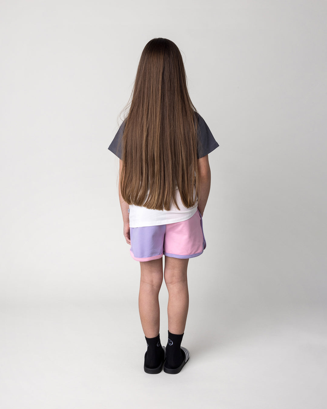 Kid wearing the Unicorn Club Tee in white and dark grey with the Sprint Short in pink, purple and aqua, back view