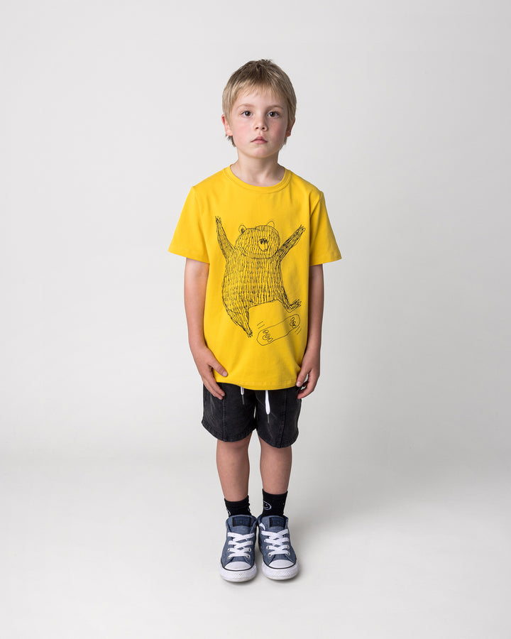 Kid wearing the Boarding Bear Tee in mustard with the Blasted Panel Short in black wash, front view