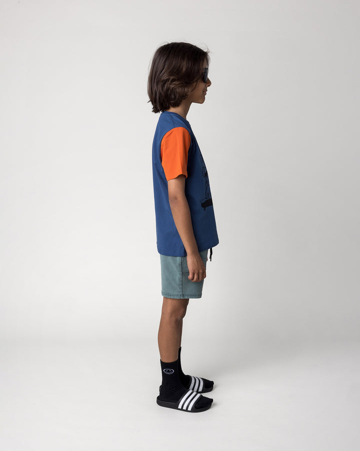 Kid wearing the Chill Mates Tee in midnight, orange and forest with the Blasted Track Short in forest wash, side view