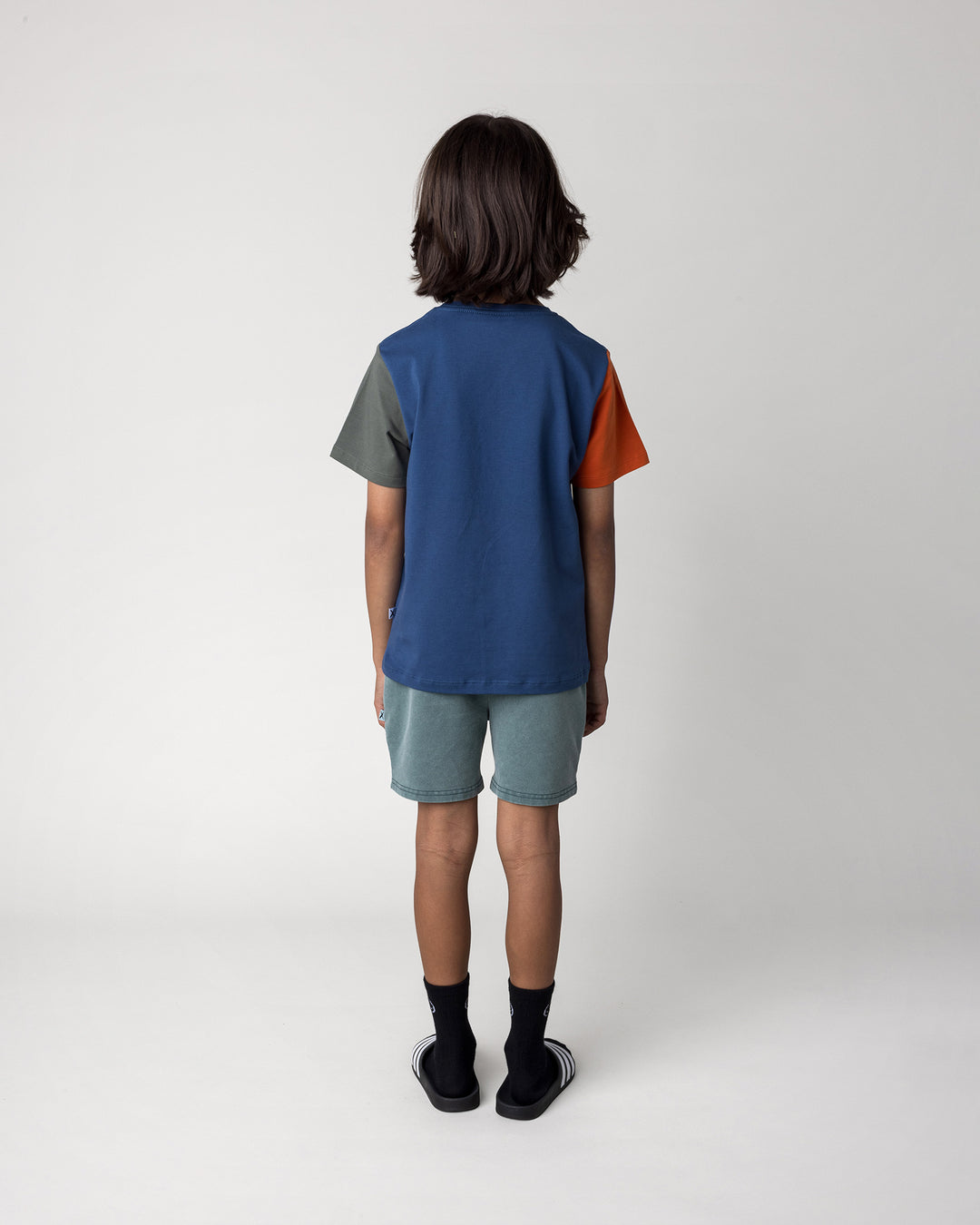 Kid wearing the Chill Mates Tee in midnight, orange and forest with the Blasted Track Short in forest wash, back view