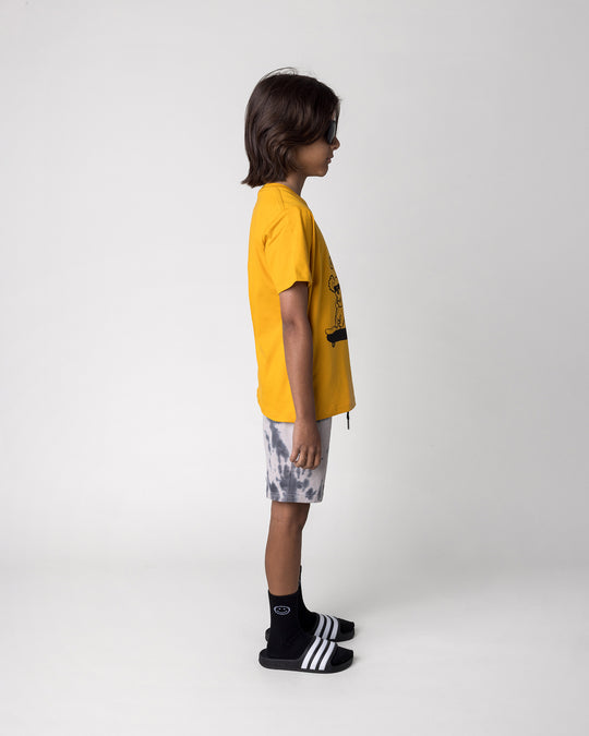 Kid wearing the Chill Mates Tee in mustard with the Splatter Short in grey, side view