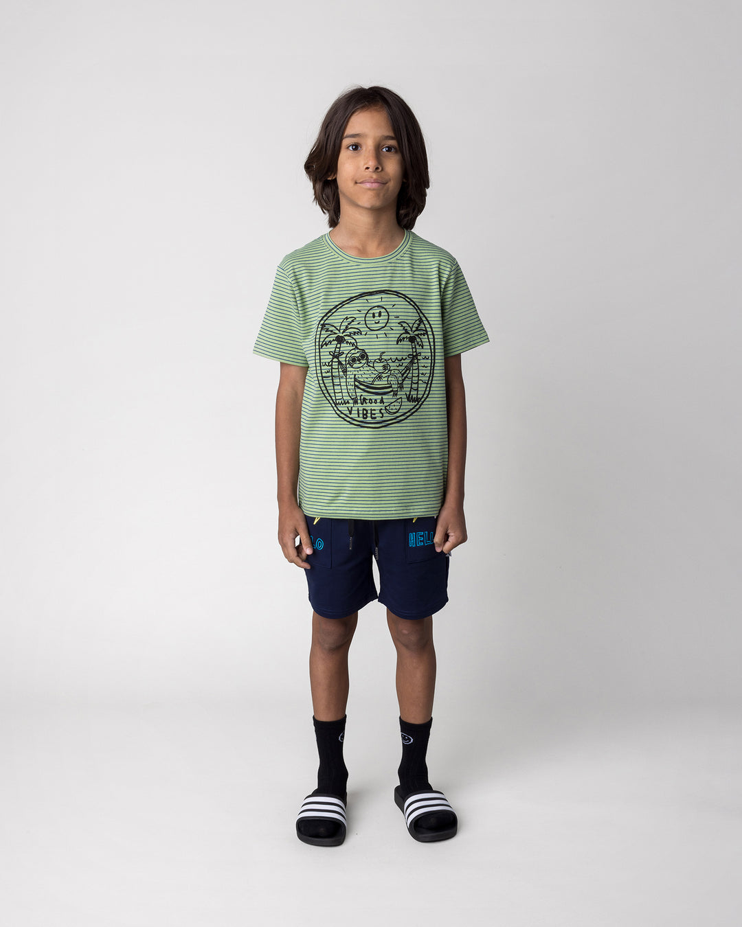 Kid wearing the Chill Sloth Tee in lime stripe with the Badges Short in ink, front view