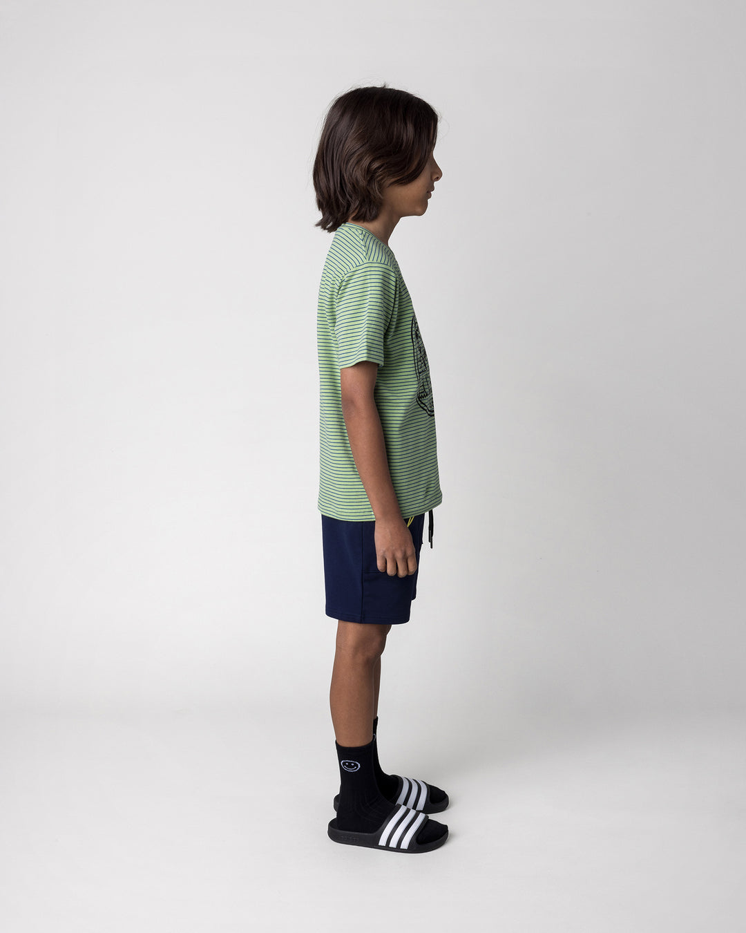 Kid wearing the Chill Sloth Tee in lime stripe with the Badges Short in ink, side view