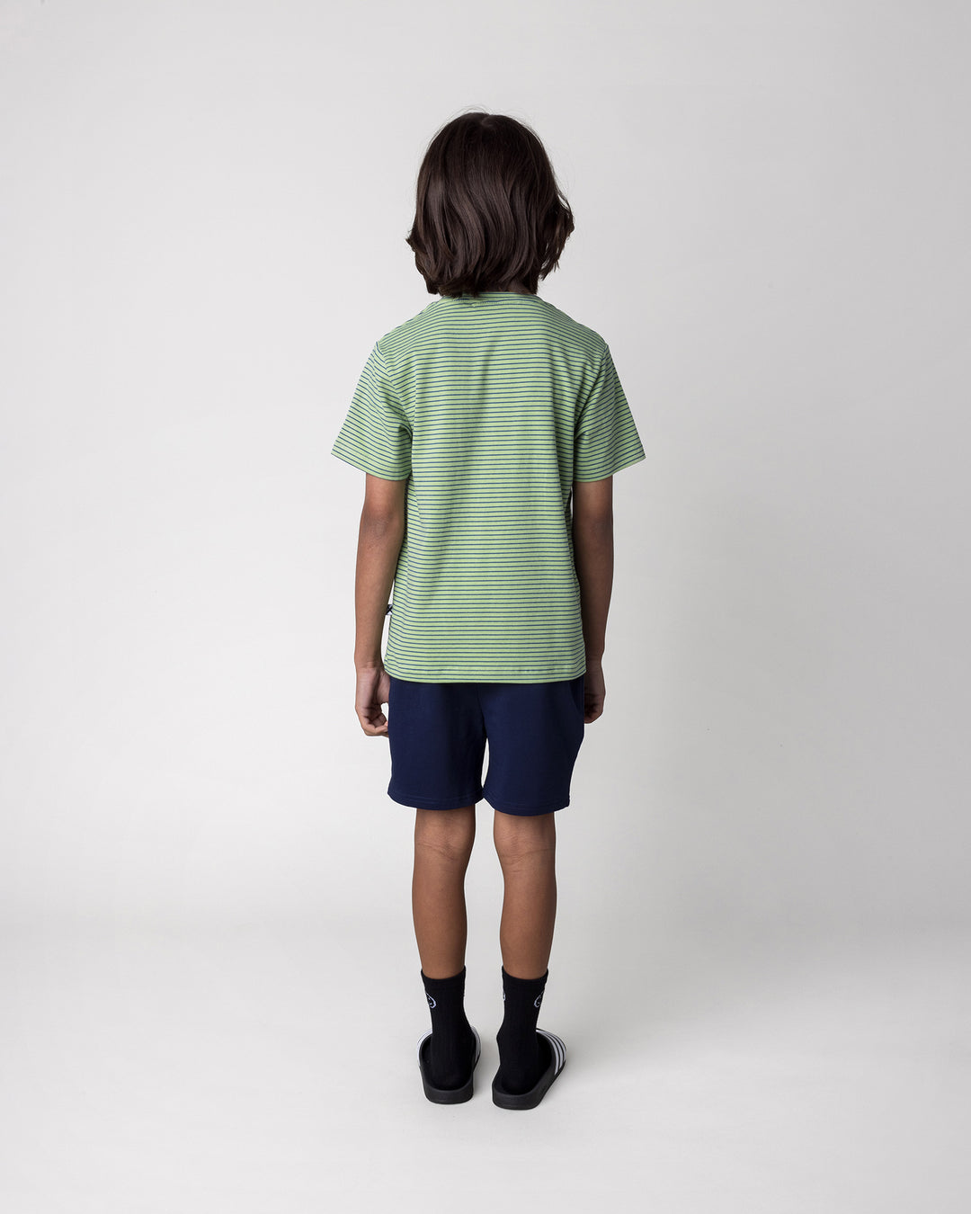 Kid wearing the Chill Sloth Tee in lime stripe with the Badges Short in ink, back view
