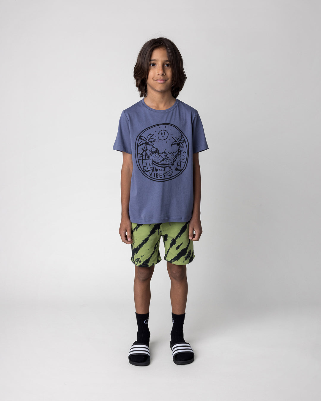 Kid wearing the Chill Sloth Tee in muted blue with the Strike Short in lime, front view