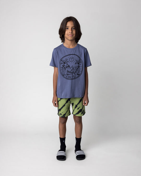 Kid wearing the Chill Sloth Tee in muted blue with the Strike Short in lime, front view