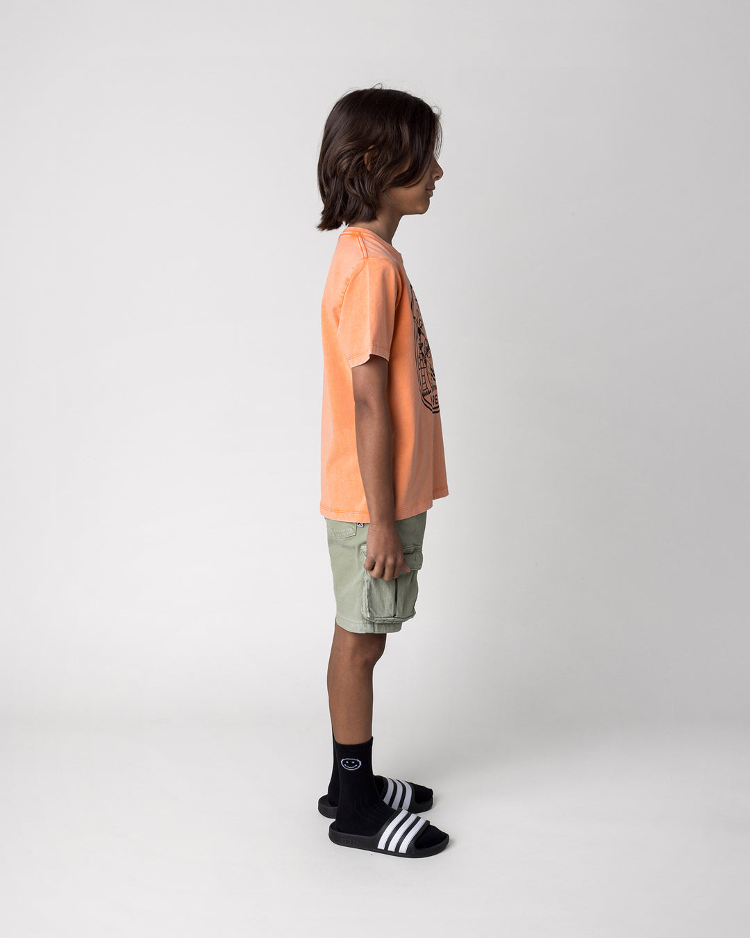 Kid wearing the Chill Sloth Tee in orange wash, side view