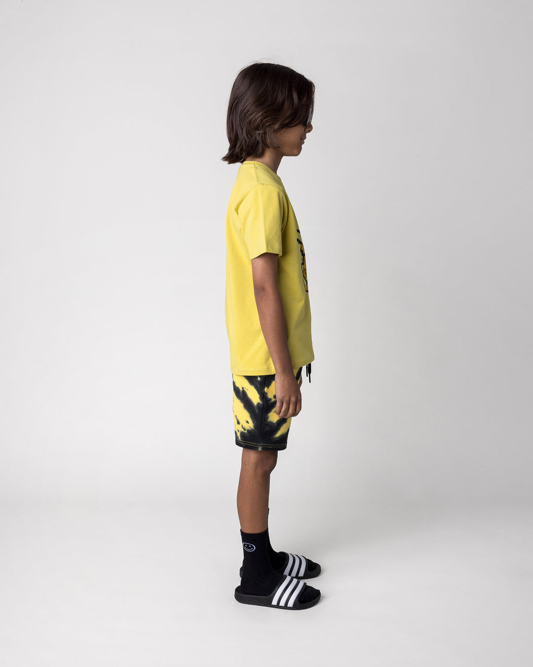 Kid wearing the Cool Dino Tee in zest with the Duo Tie Dye Short in lemon and rust, side view